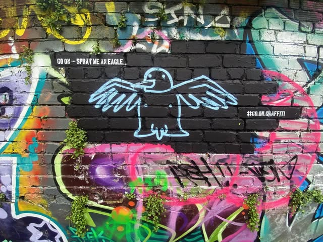 A stencilled prompt reading 'GO ON - SPRAY ME AN EAGLE' on a Bristol wall